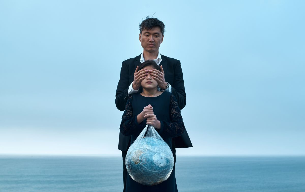 Un padre y una hija que aguanta un globo terráqueo que está rodeado de plástico / PEXELS