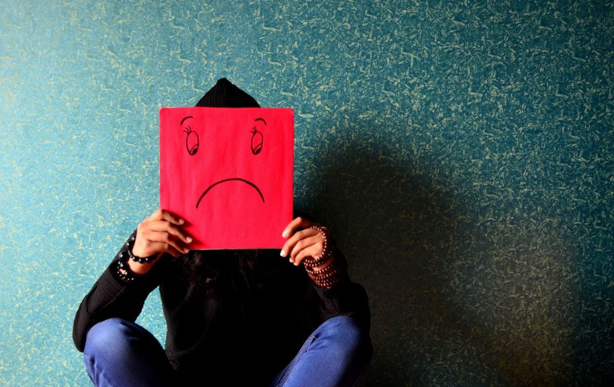 Una persona con depresión muestra su estado de ánimo con una cara triste en una cartulina roja / PIXABAY