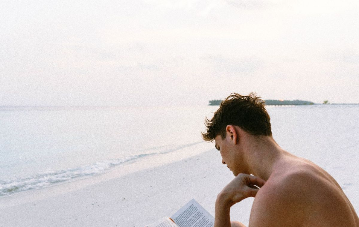 Un joven lee un libro en la playa / PEXELS