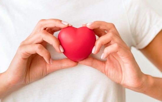 Una mujer que quiere bajar el colesterol, con un corazón de plástico entre las manos / FREEPIK