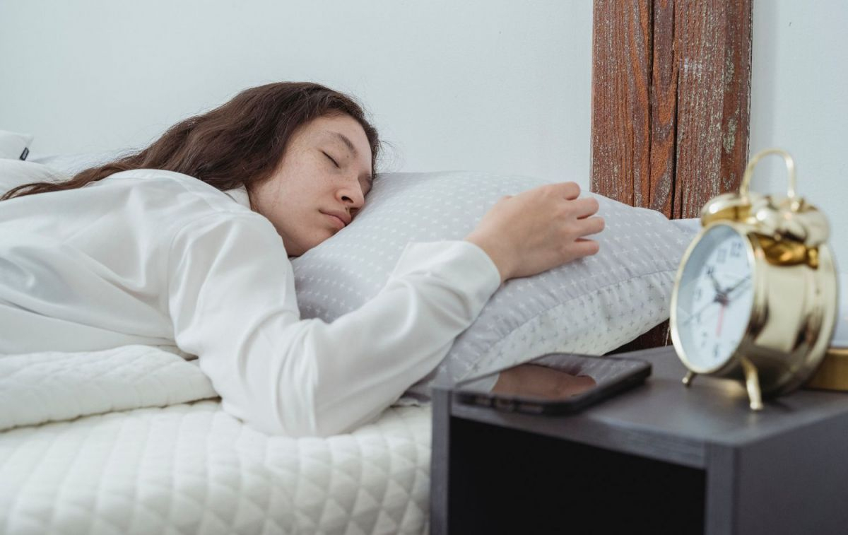 Una mujer en la cama, junto al móvil y un despertador / PEXELS