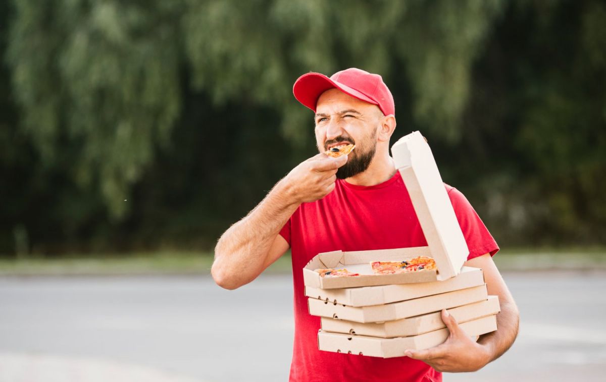 Un repartidor come un trozo de pizza que está en una caja de cartón / FREEPIK