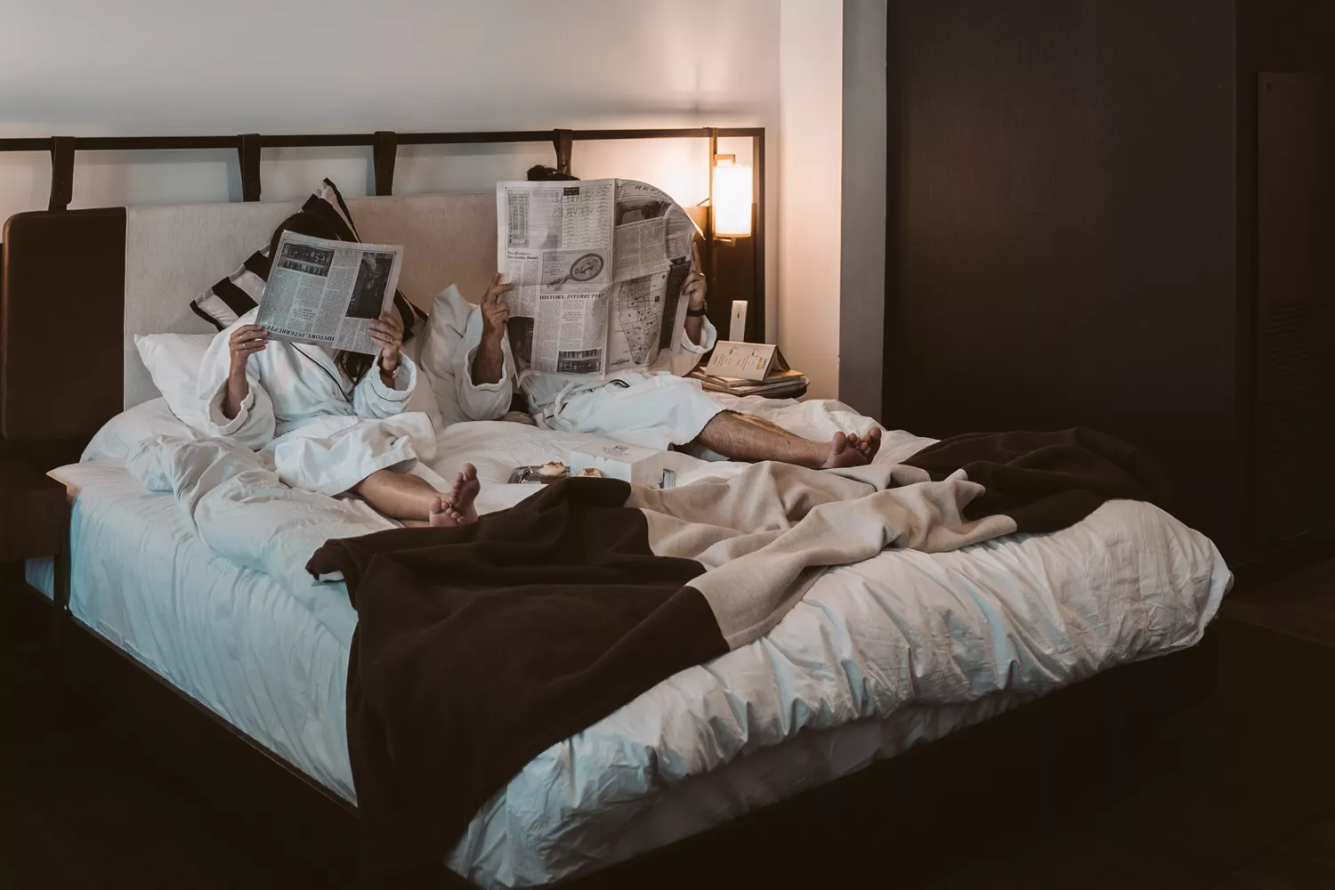 Dos huéspedes leen la prensa en una cama de hotel / PEXELS