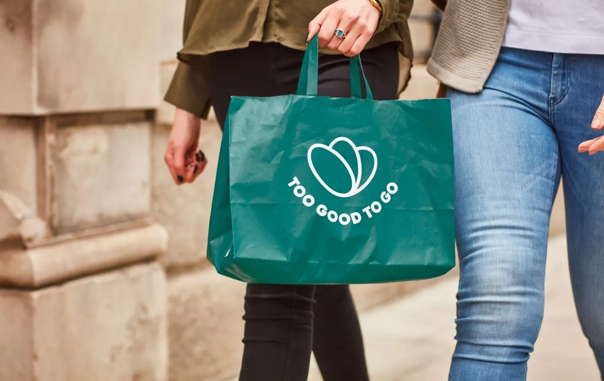 Dos personas llevan una bolsa de papel de Too Good To Go / TOO GOOD TO GO Dos personas llevan una bolsa de papel de Too Good To Go / TOO GOOD TO GO