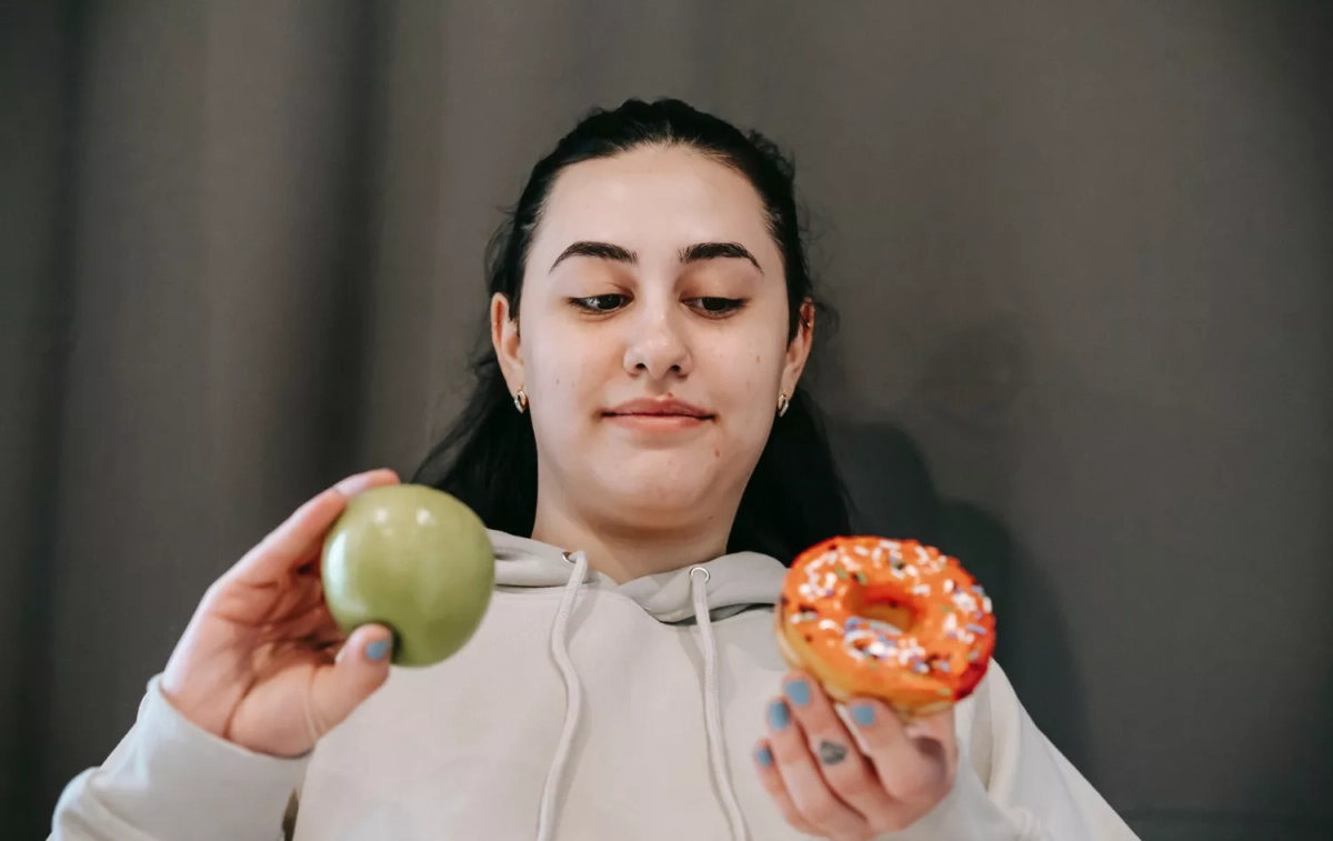 Una persona con una manzana y un dulce lleno de azúcar en sus manos / PEXELS