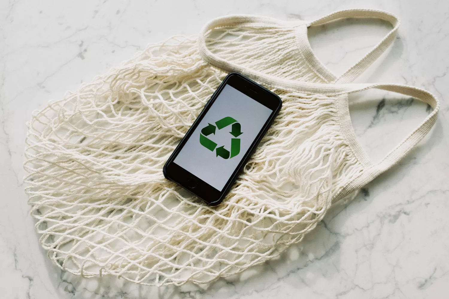 Un móvil con un logo verde y una bolsa sostenible PEXELS