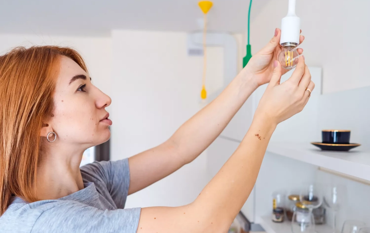 Una mujer instala una bombilla de bajo consumo para ahorrar en la factura de la luz / FREEPIK  - @teksomolika