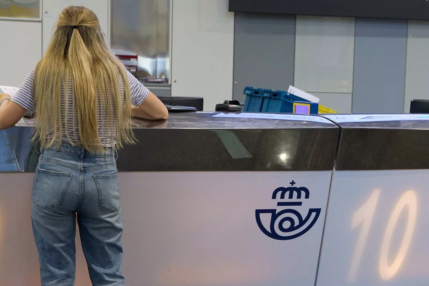 Una chica en el mostrador de la oficina de Correos sin que le atienda nadie de atención al cliente  