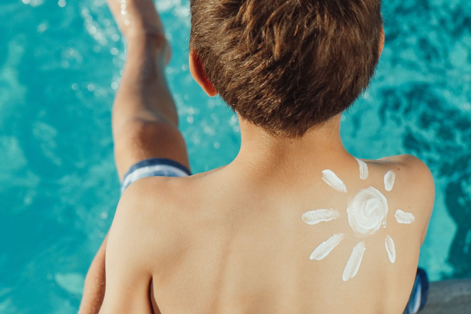 Un niño en la piscina con un sol dibujado con crema solar / PEXELS