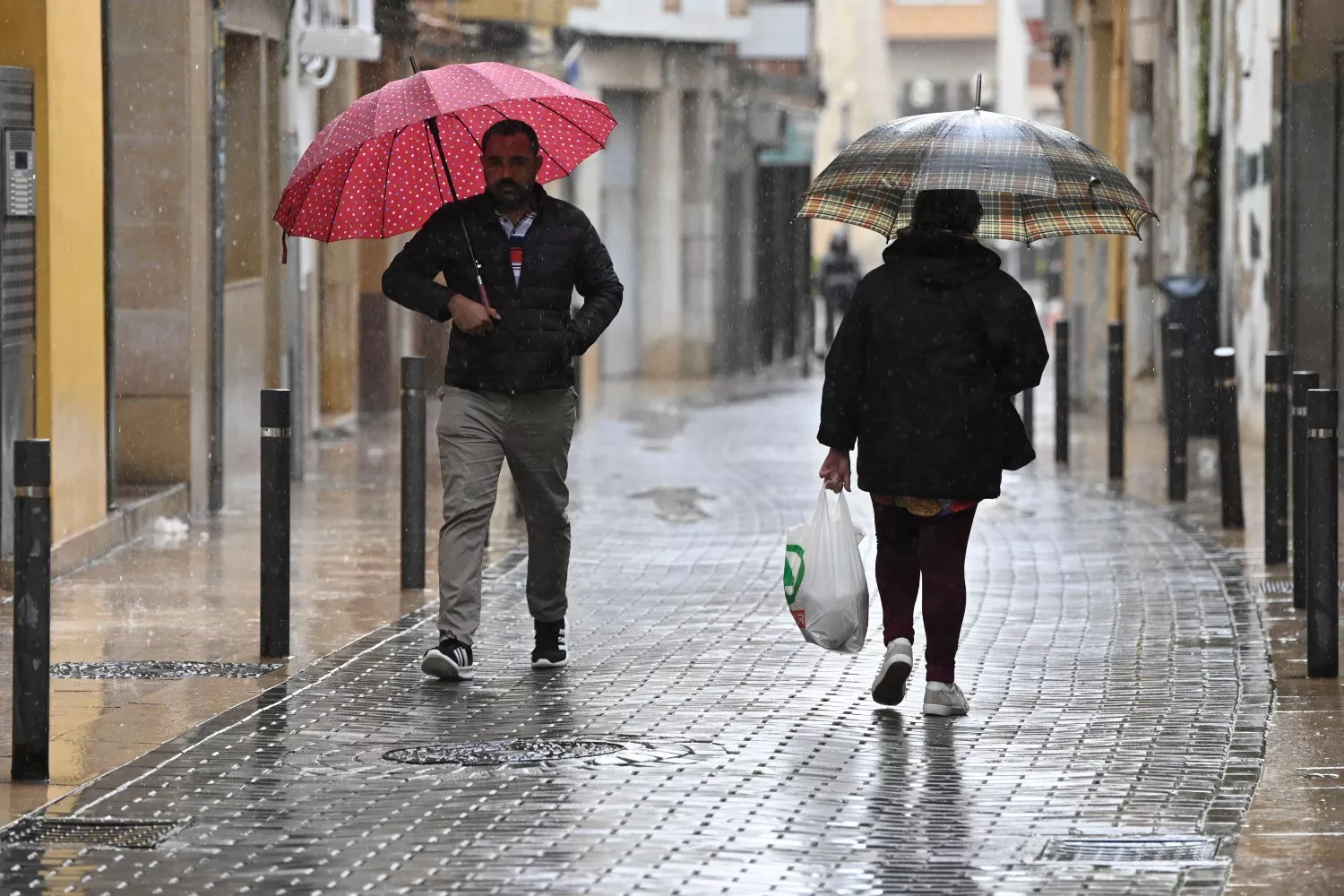 Unos viandantes se protegen de la lluvia con paraguas y luego pondrán la calefacción en casa   Andr