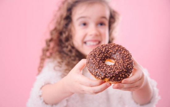 Una niña con un donut, un alimento ultraprocesado / FREEPIK Una niña con un donut, un alimento ultraprocesado / FREEPIK