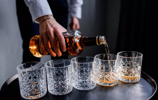 Un camarero sirve varios vasos de whisky de una botella sin dosificador / FREEPIK Un camarero sirve varios vasos de whisky de una botella sin dosificador / FREEPIK