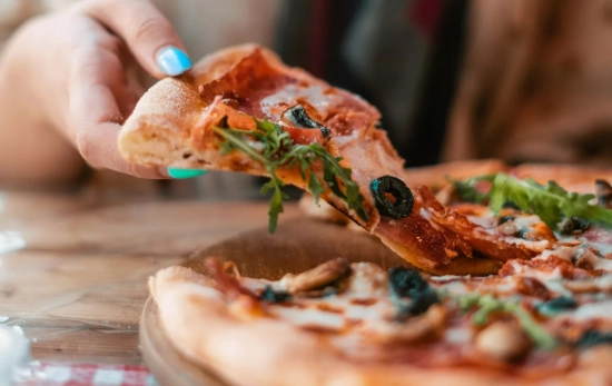 Una persona con un trozo de pizza / PEXELS Una persona con un trozo de pizza / PEXELS