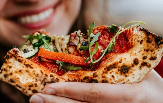 Una chica con un trozo de pizza / PEXELS Una chica con un trozo de pizza / PEXELS