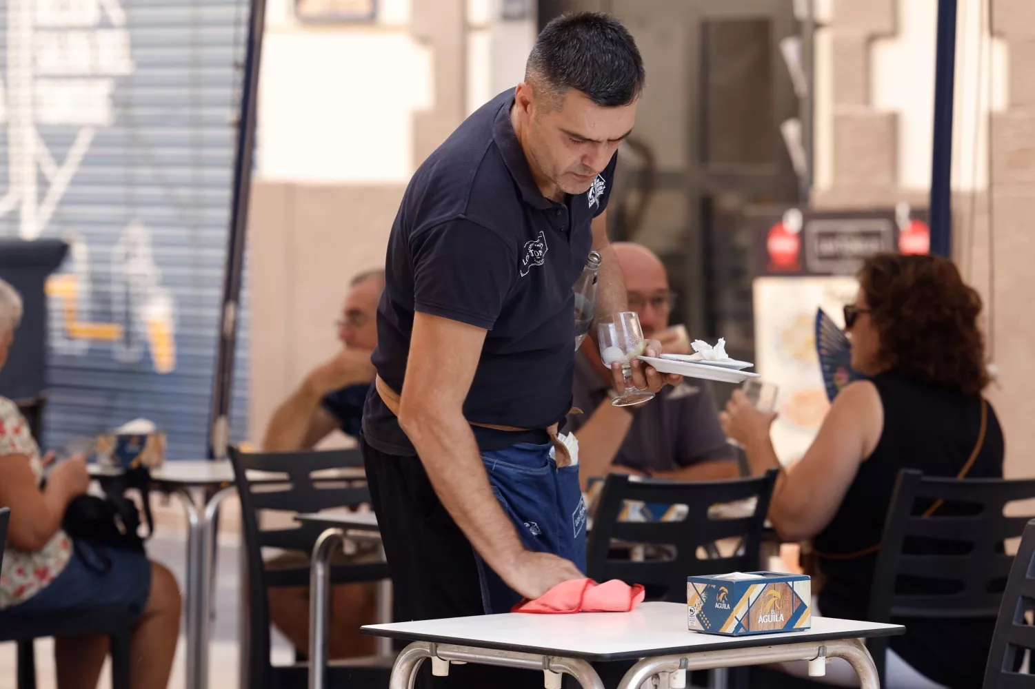 Un camarero limpia la mesa de una terraza de un bar después de que unos clientes hayan estado tomando café / Biel Aliño - EFE