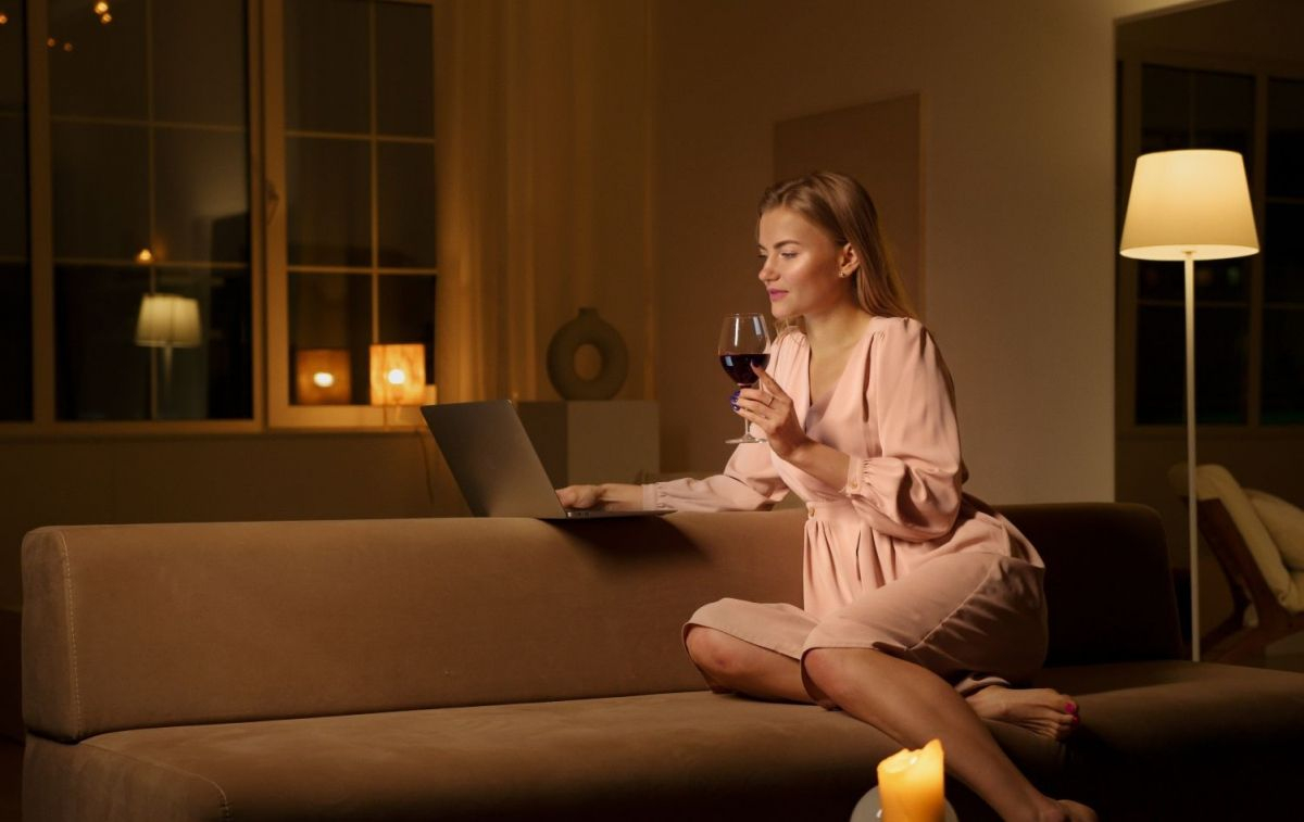 Una china sentada en el sofá tomando una copa de vino delante del ordenador / PEXELS