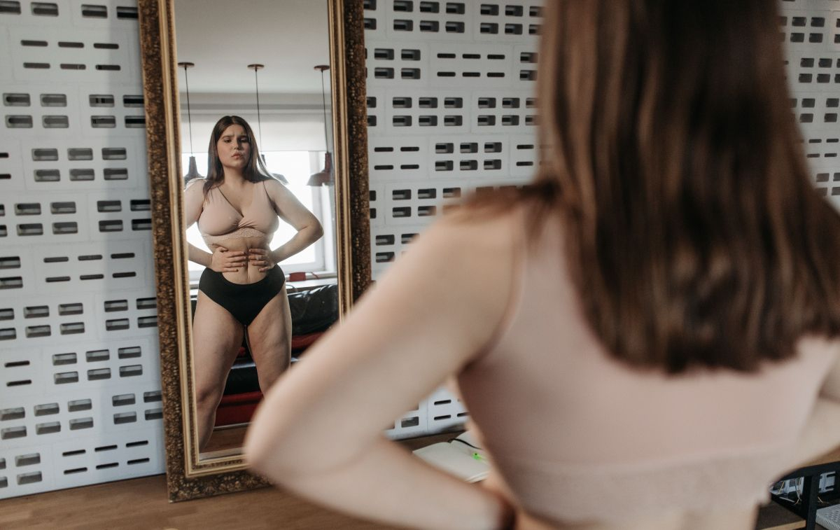 Una chica que se mira en el espejo y piensa que tiene kilos de más / PEXELS