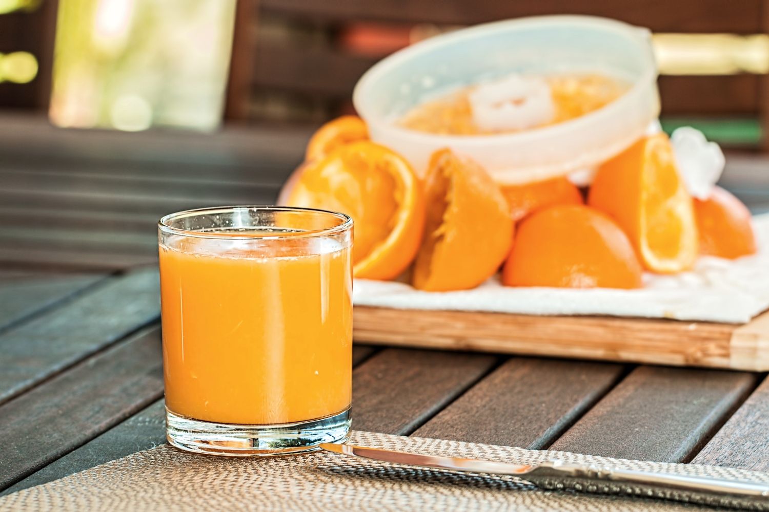 Un vaso de zumo de naranja y detrás varias piezas de naranja / PEXELS