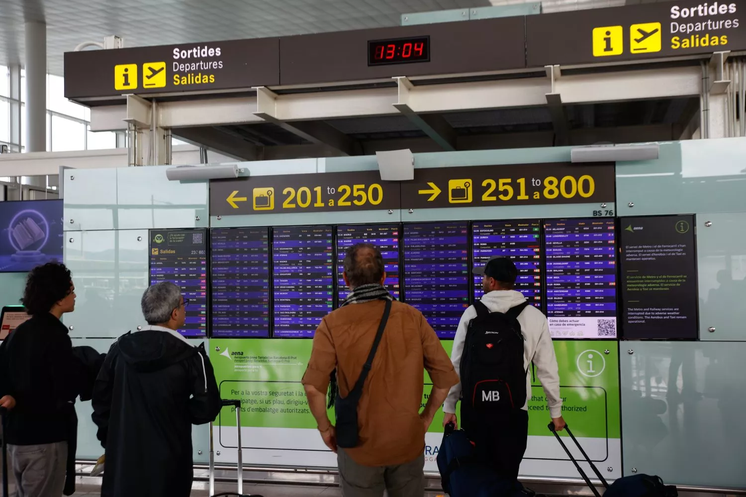Varias personas miran los paneles informativos en el aeropuerto de Barcelona El Prat