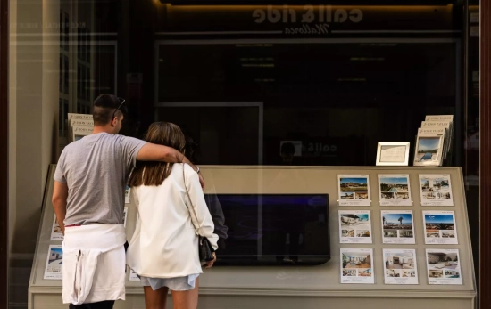 Dos personas observan los anuncios de viviendas en venta en una inmobiliaria Dos personas observan los anuncios de viviendas en venta en una inmobiliaria