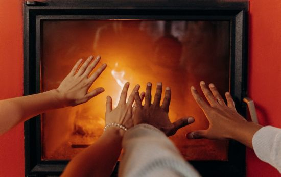 Dos personas calientan sus manos con el calor de una chimenea / PEXELS