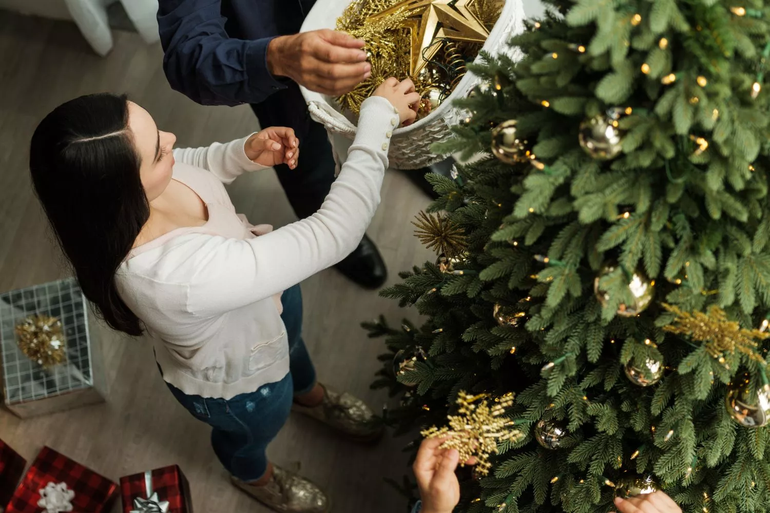 Unas personas decorando el árbol de Navidad según las tendencias de 2025/ CANVA