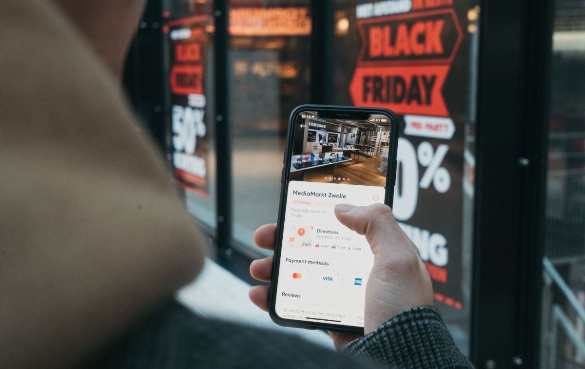 Un comprador mira su móvil frente a un local con publicidad de Black Friday / Unsplash