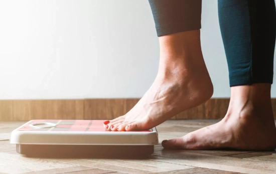 Una chica subiéndose a la báscula/ CANVA