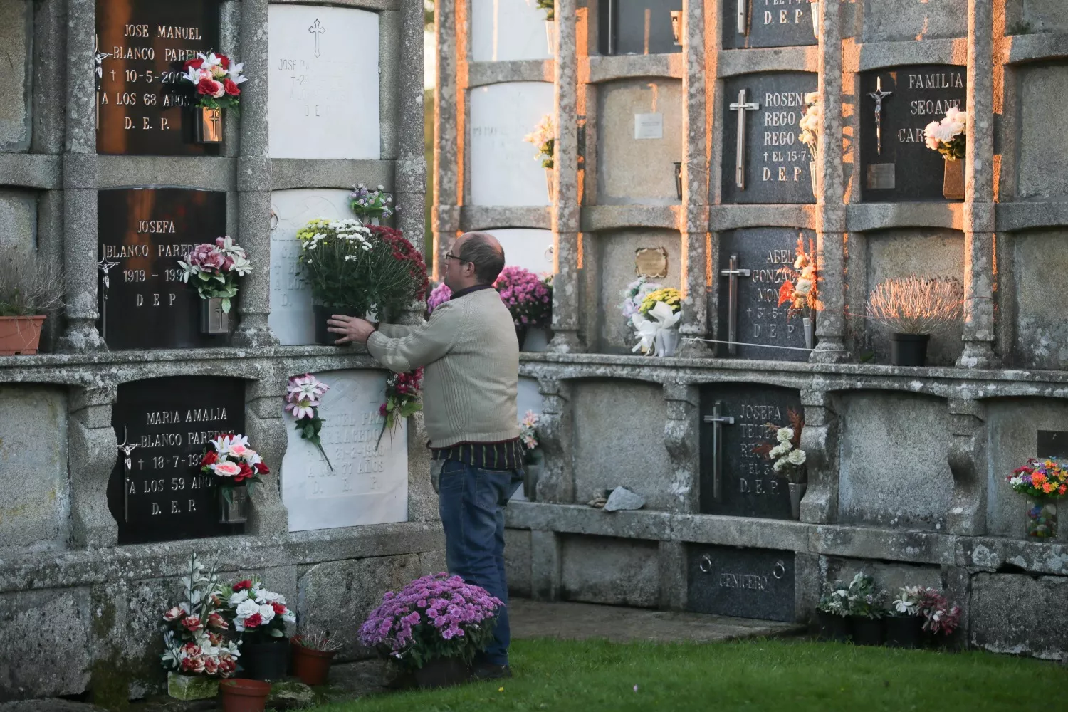 Un hombre pone flores en un nicho del cementerio   Carlos Castro   EP