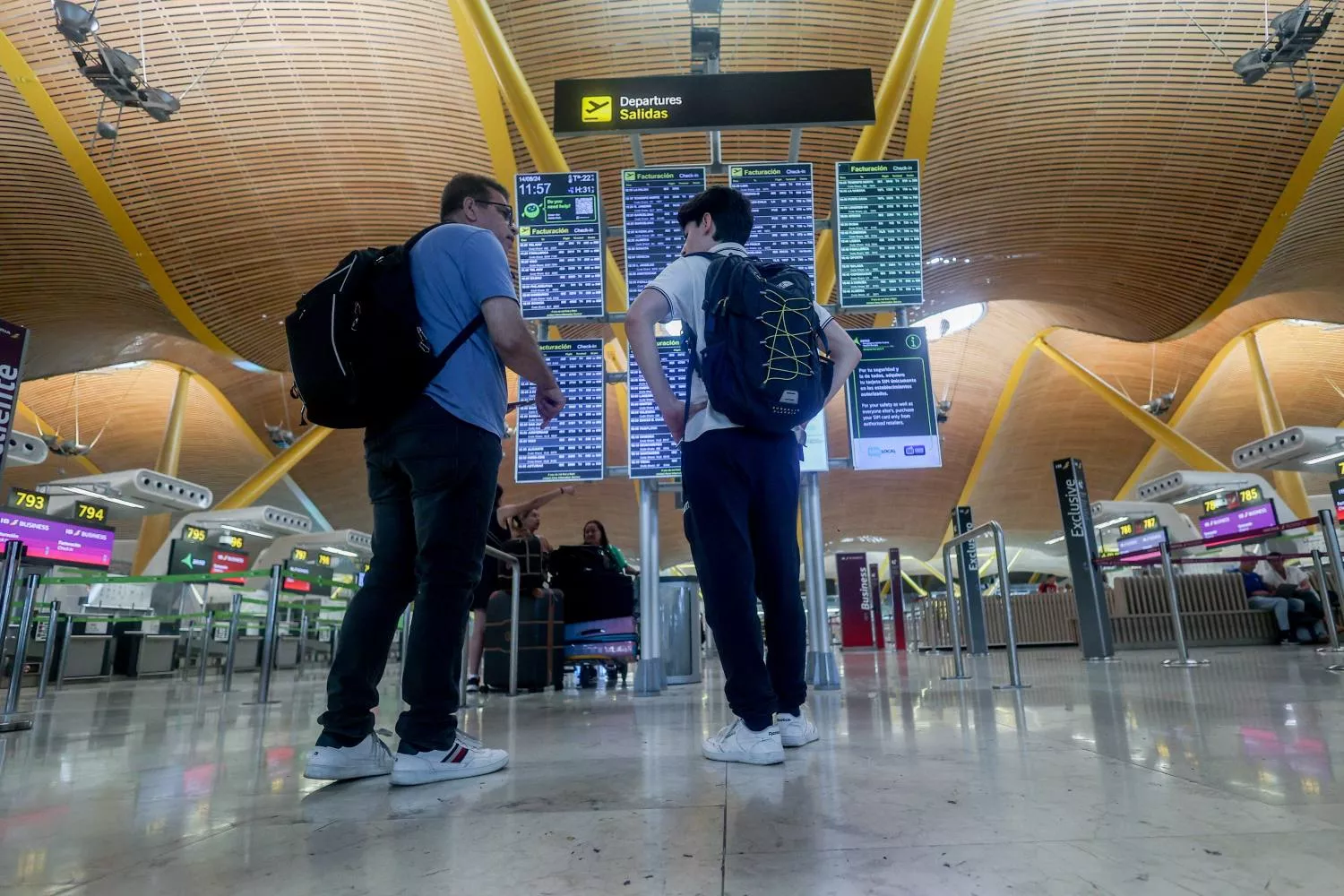 Dos personas consultan el estado de los vuelos en un panel de información del aeropuerto de Madrid / EP