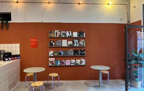 Una estantería con libros y un par de mesas con taburetes en Stamina / TC