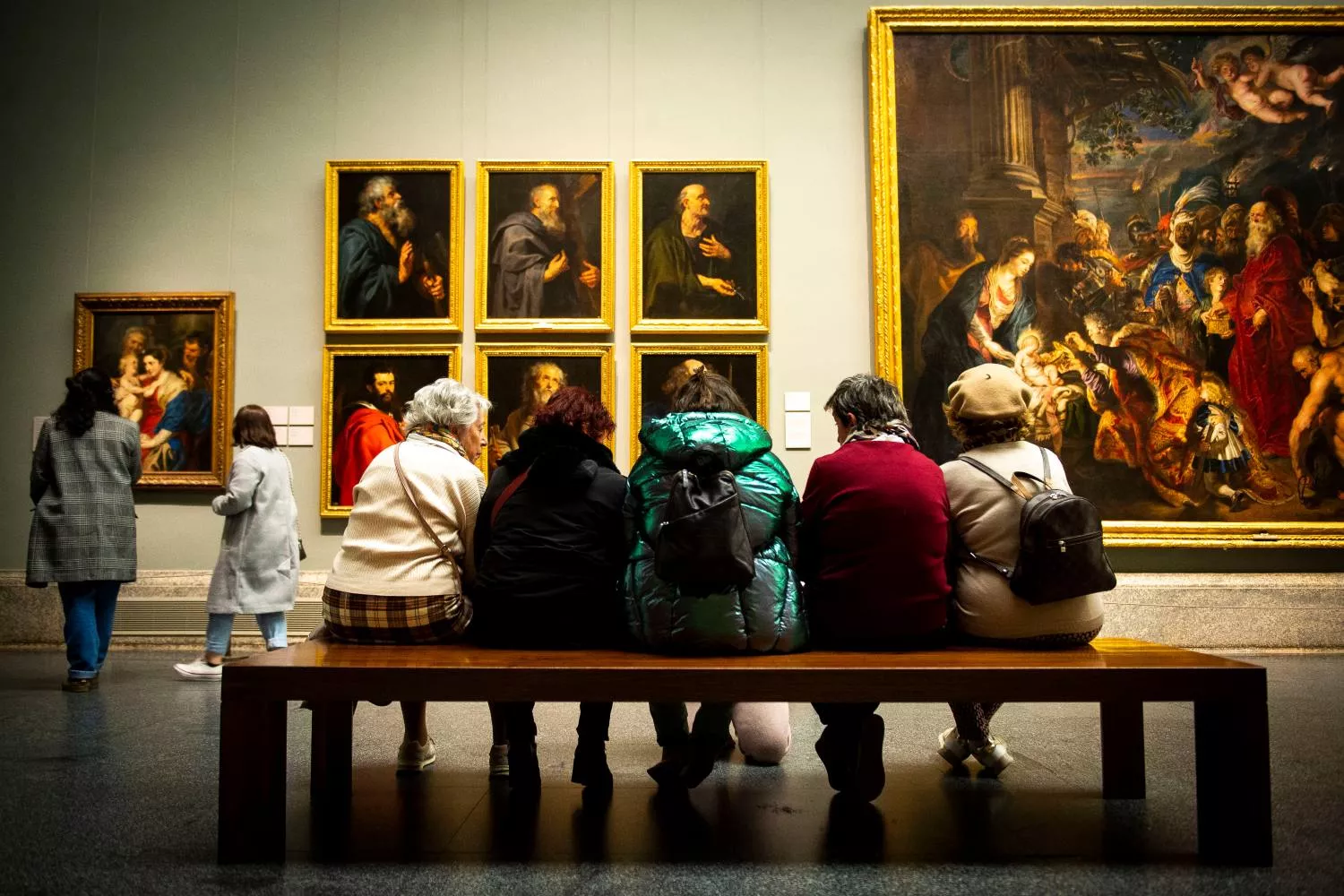 Varias personas se sientan mientras observan cuadros en el Museo del Prado de noche