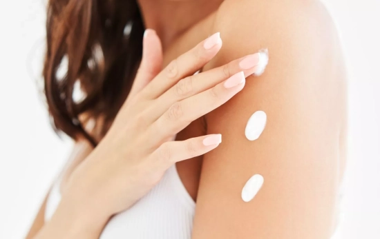 Una mujer echándote la crema corporal/ CANVA