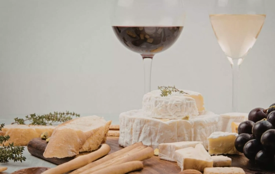 Una tabla de quesos acompañada de dos copas de vino/ CANVA