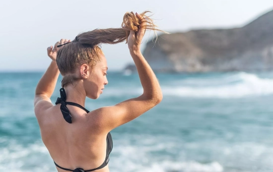 Una chica recogiéndose el pelo en la playa/ CANVA Una chica recogiéndose el pelo en la playa/ CANVA