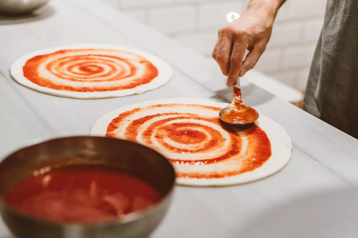 Una persona añade tomate a unas bases de pizza   PEXELS