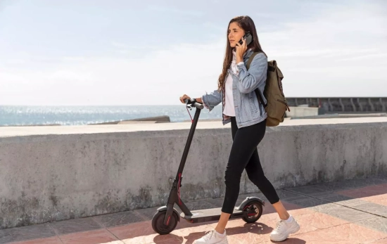 Una mujer camina por la calle con su patinete eléctrico / FREEPIK