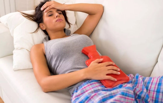 Una mujer aplicándose calor en la zona abdominal para aliviar el dolor menstrual/ CANVA