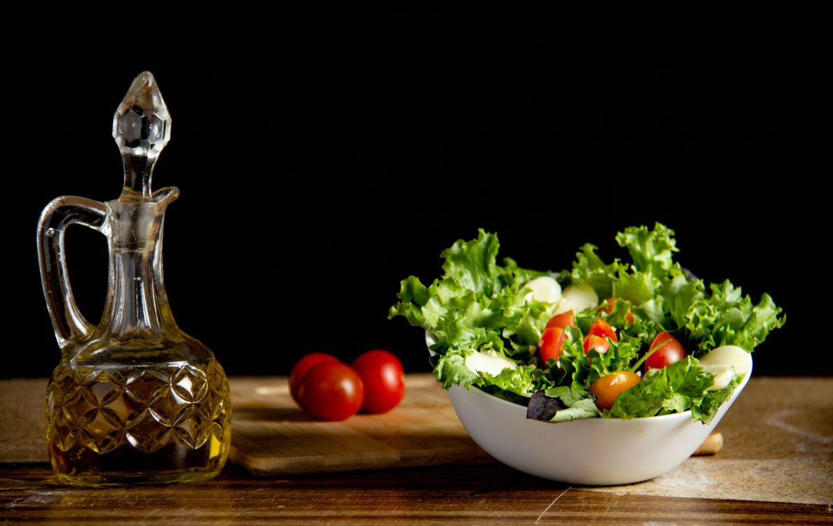 Una jarra de aceite de oliva junto a un bol de ensalada encima de una mesa / PEXELS