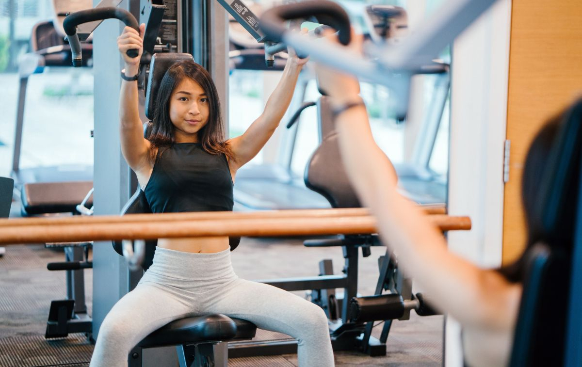 Una mujer hace ejercicios de pecho en una máquina del gimnasio / PEXELS