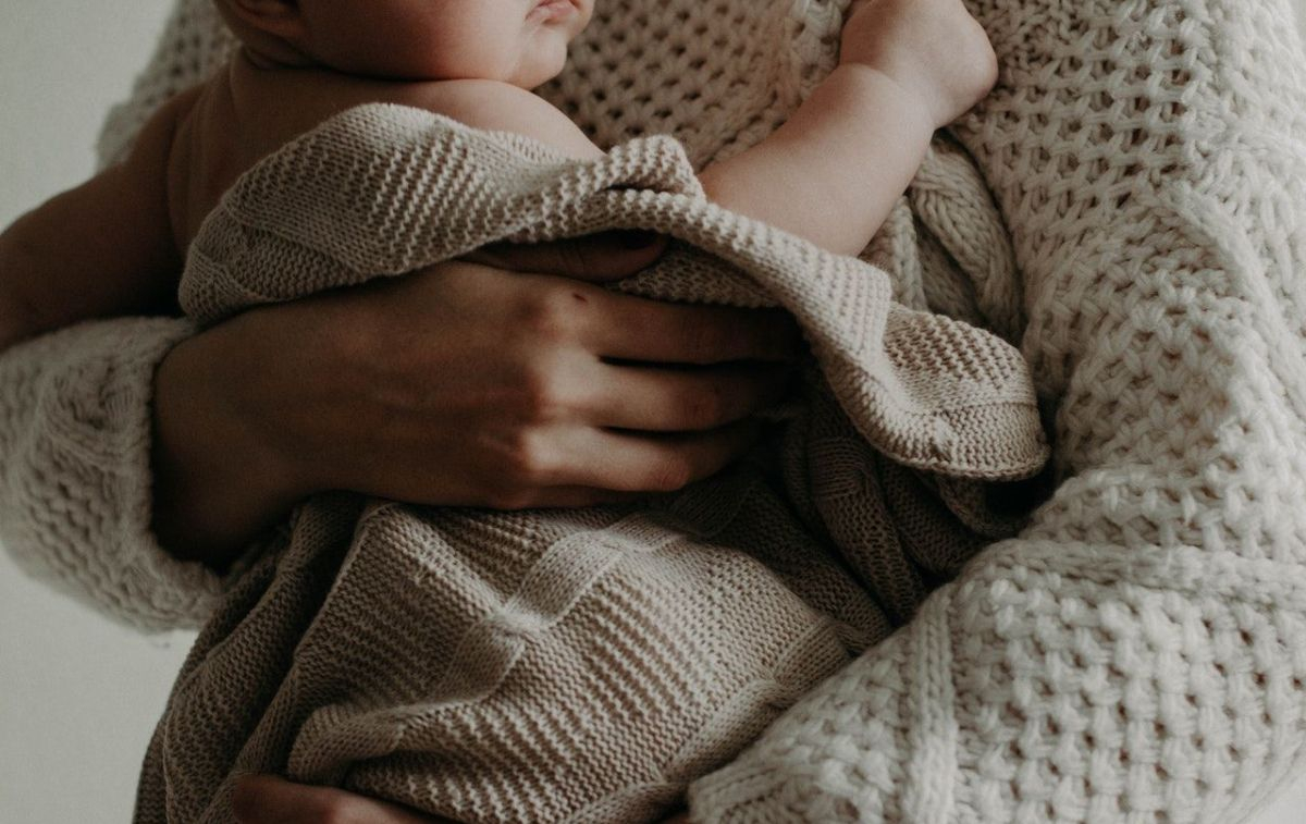 Un bebé sobre el brazo de su madre / PEXELS 